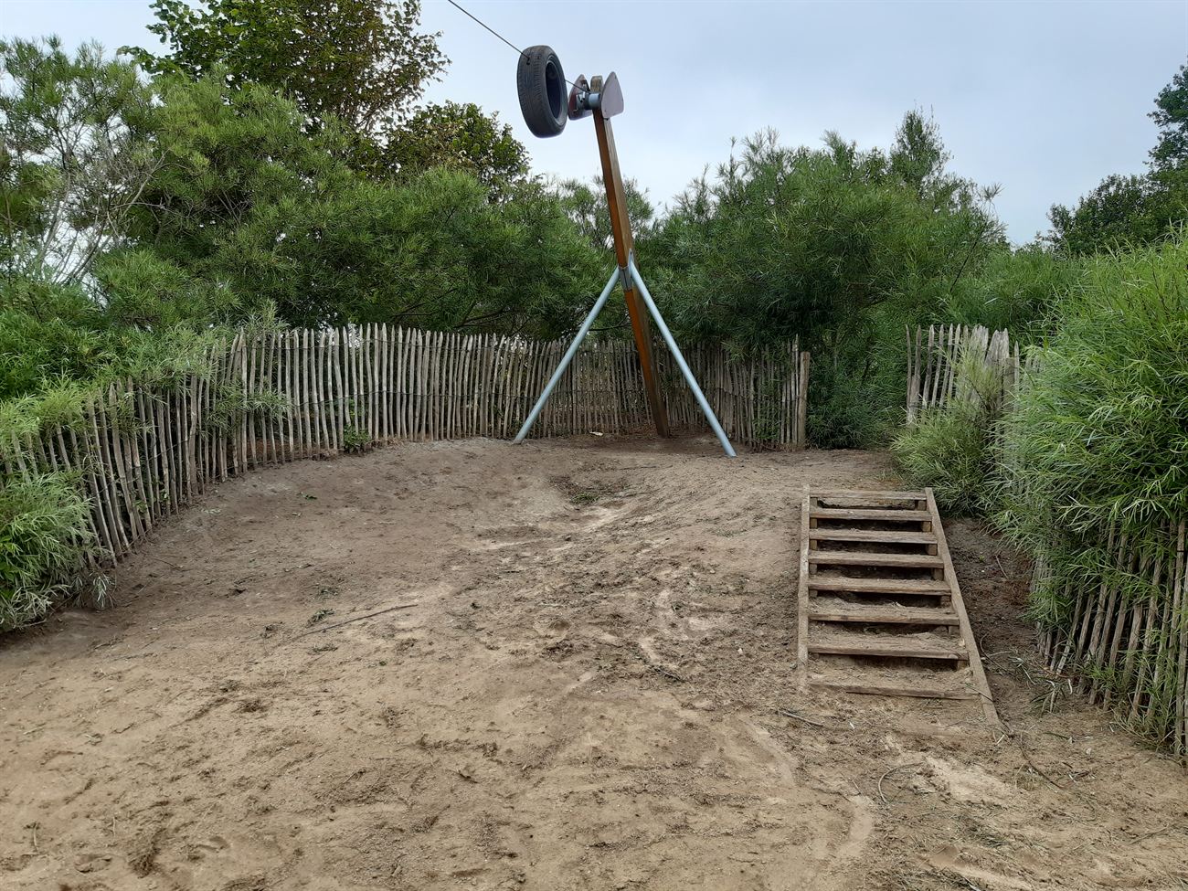 Speelzone met zand, hekwerk, struiken en bomen